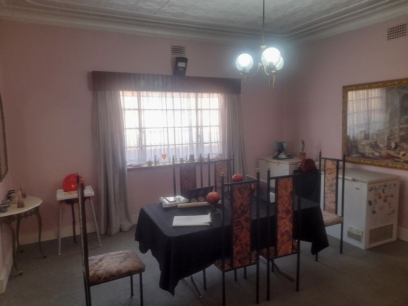 A dining room featuring decorative ceiling cornices, a central chandelier, and a window pelmet, offering a traditional layout with potential for modern updates.