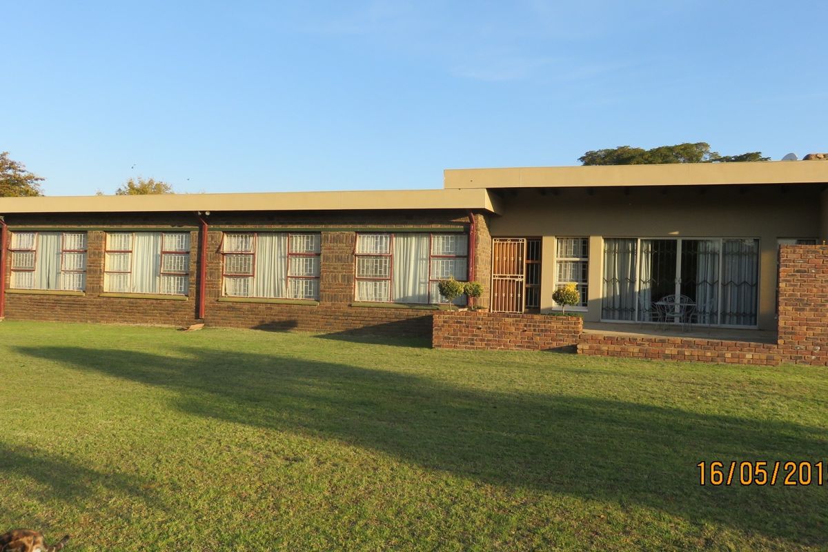 Rear view of a face-brick small holding residence featuring a large lawn, concrete patio area, and sliding glass doors with security gates.