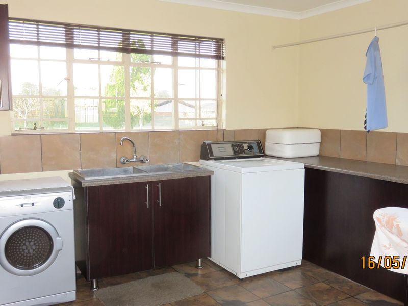 Functional laundry room featuring built-in cabinetry, a double basin sink, tiled backsplash, and dedicated space for washing machines.