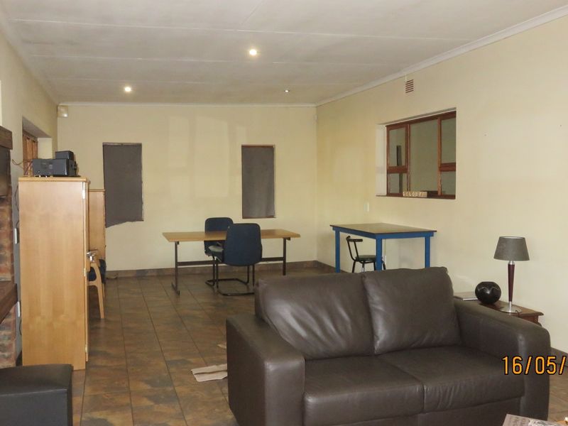 Spacious living area featuring a brick fireplace and tiled flooring, offering a versatile layout with potential for modernization and improved lighting.