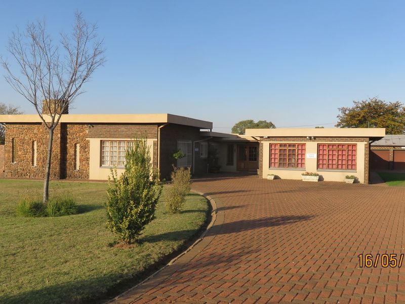 Front elevation of a small holding property featuring a brick driveway, stone-clad exterior walls, and a flat roof design.