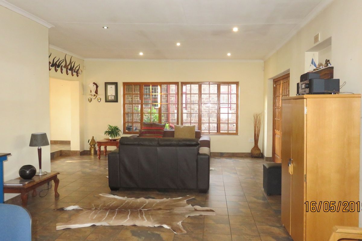 Spacious living room featuring tiled flooring, recessed downlighting, and large wooden-framed windows allowing natural light into the area.