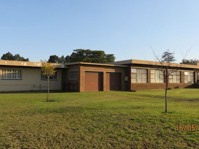 Rear view of a single-story brick property featuring a double garage with roller shutter doors and expansive windows overlooking a large lawn.