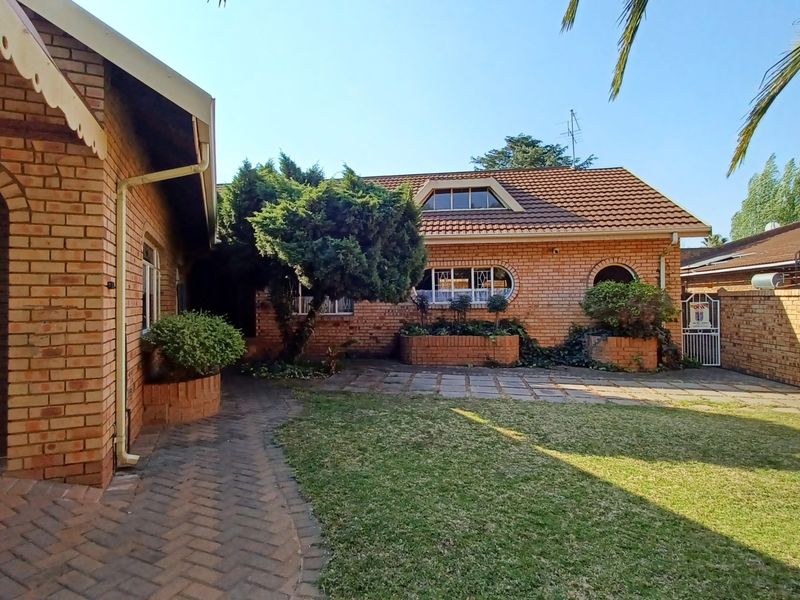A well-maintained rear exterior view featuring a face brick house, paved patio area, established garden, and a garage.