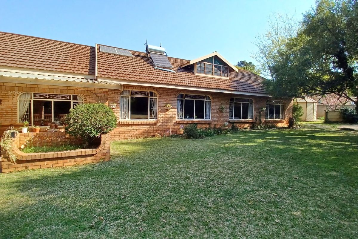 Rear view of a traditional brick house featuring a tiled roof, solar water heating system, and a well-maintained garden lawn.