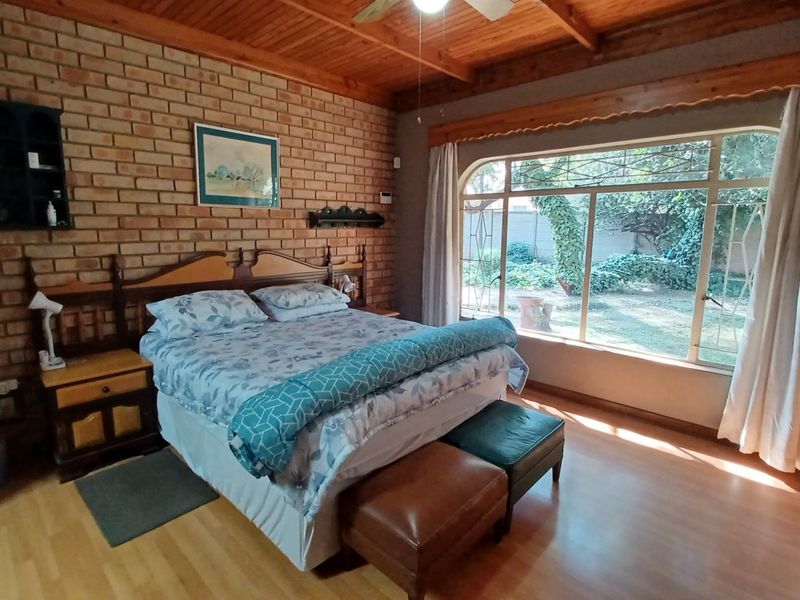 Spacious bedroom featuring an exposed brick feature wall, timber beam ceiling, and large window overlooking the garden.