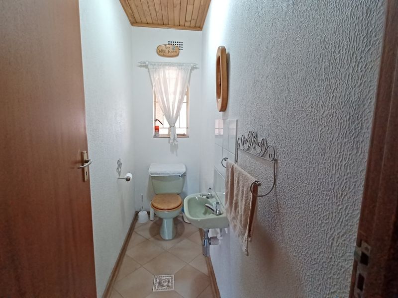 A compact guest bathroom featuring a wall-mounted basin, toilet, tiled flooring, and a timber-paneled ceiling.