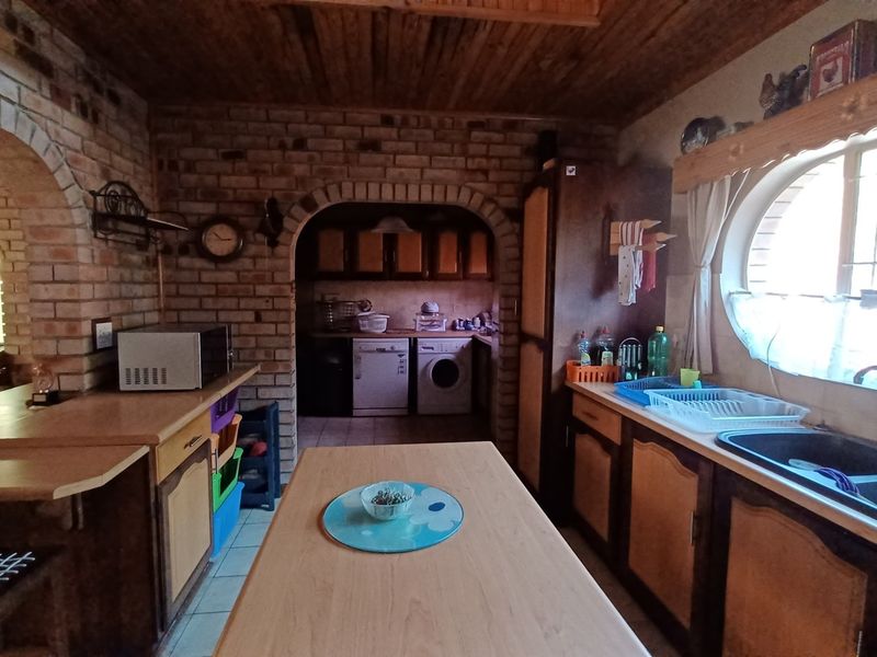 A rustic kitchen featuring exposed brick walls, timber ceiling, arched architectural details, and built-in cabinetry with a double basin sink.