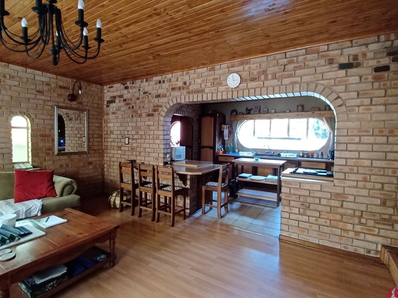 Open plan living and kitchen area featuring exposed brick walls, timber ceiling, and a functional kitchen layout with a convenient pass-through counter.