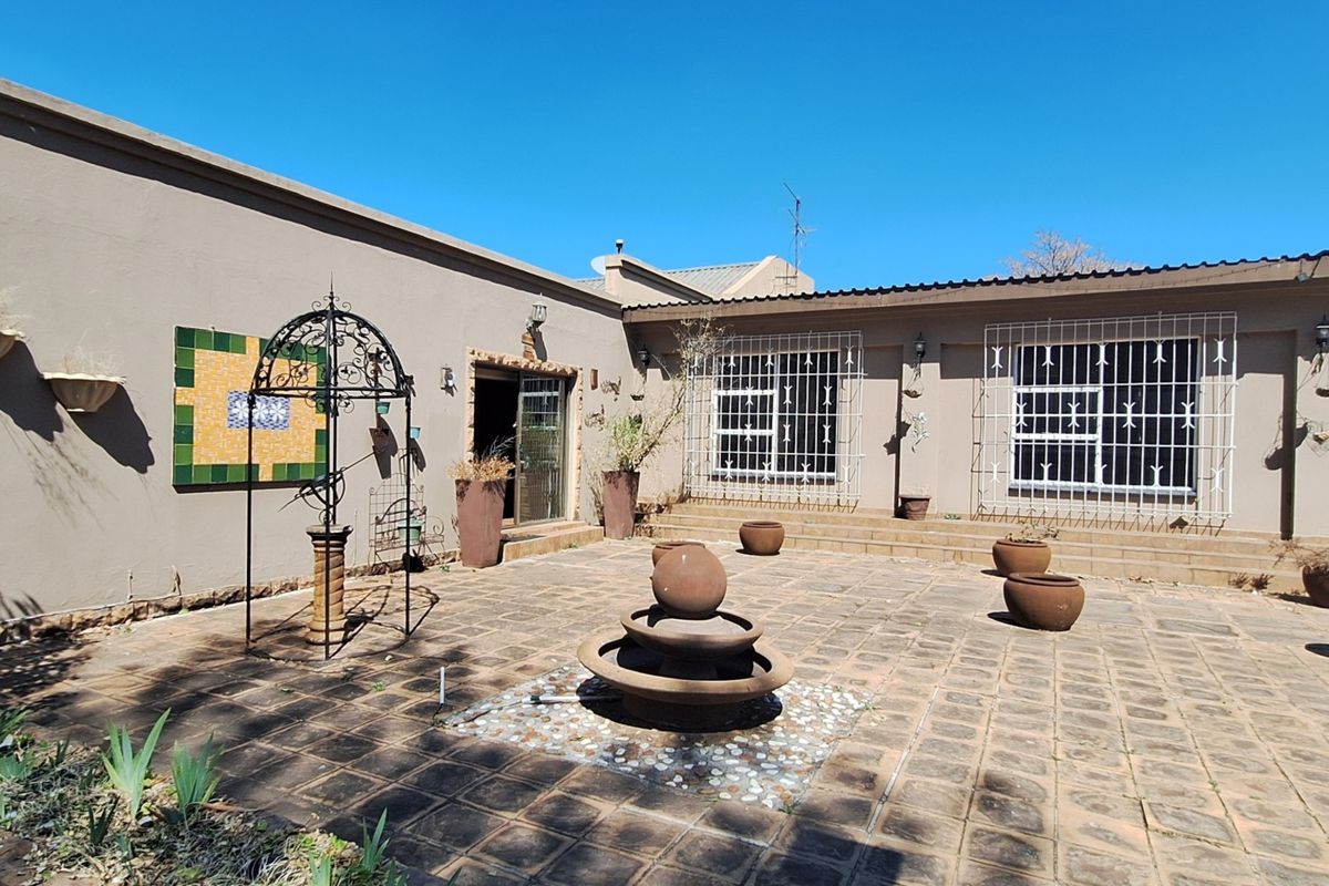 A spacious rear paved patio area featuring a central stone water fountain, security-fitted windows, and direct access to the main dwelling.
