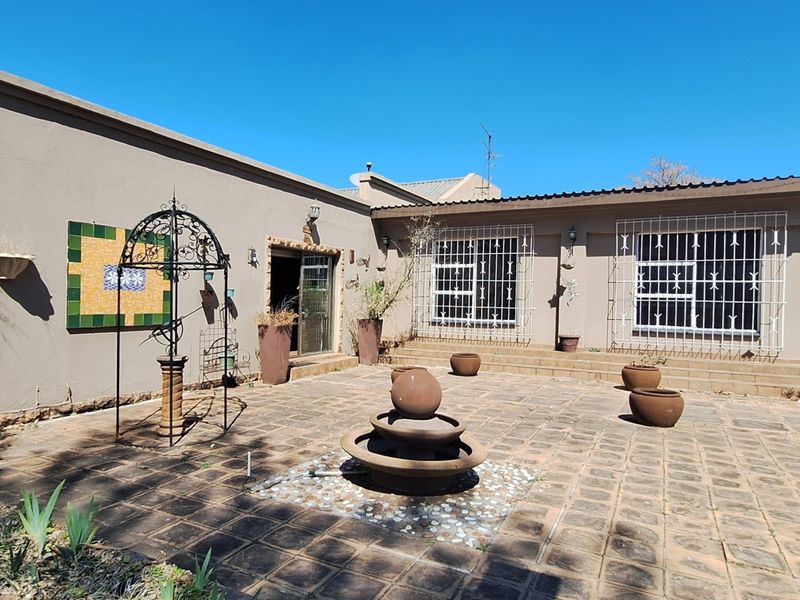 A spacious rear paved patio area featuring a central stone water fountain, security-fitted windows, and direct access to the main dwelling.