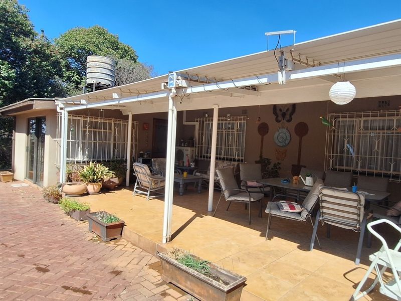 A covered outdoor patio area featuring tiled flooring, security bars on windows, and direct access to the paved garden space.