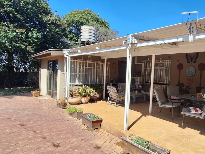A covered outdoor patio area featuring brick paving, tiled flooring, and security bars on the windows, overlooking a garden space.