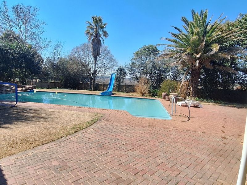 Outdoor pool area featuring a swimming pool with a slide, surrounded by brick paving and adjacent to a covered patio space.