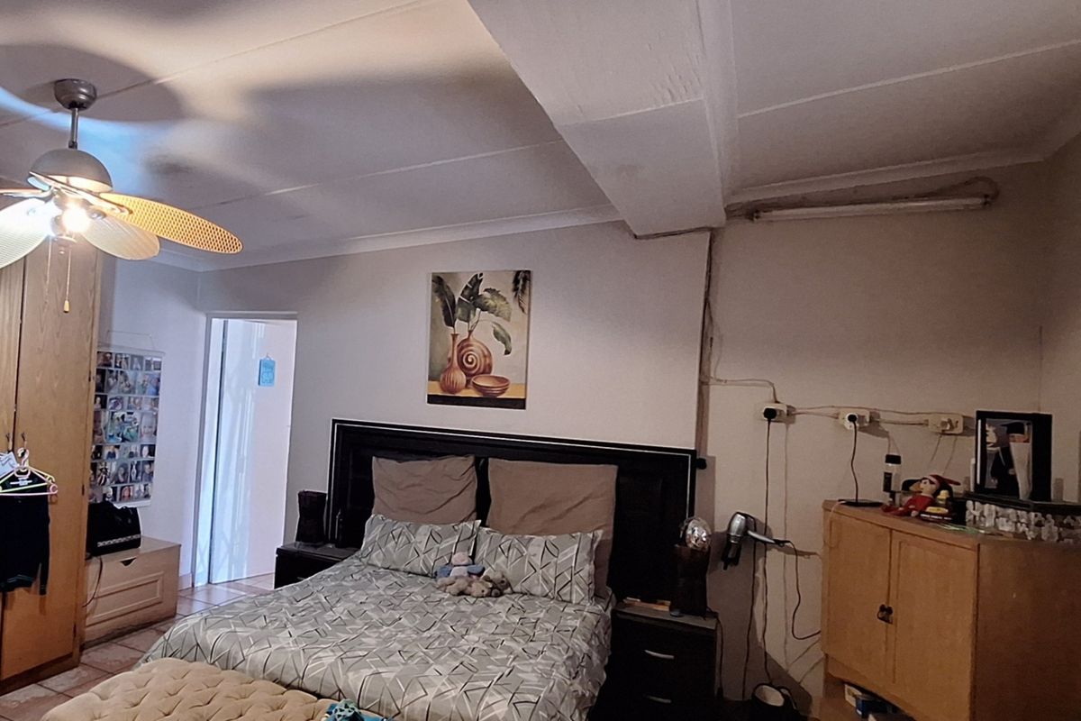 A bedroom featuring built-in cupboards, a ceiling fan, and tiled flooring, requiring some cosmetic updates to the electrical finishes and ceiling.