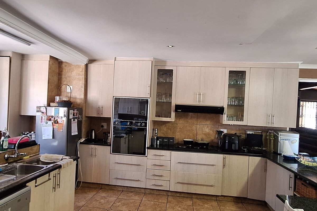 A functional kitchen featuring light wood cabinetry, granite countertops, built-in oven, extractor fan, and tiled flooring with ample storage space.
