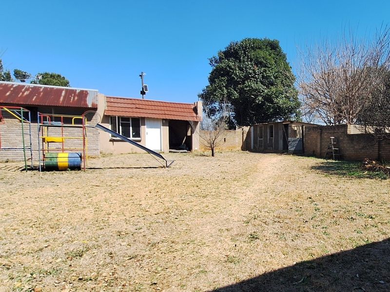 Rear garden area featuring a brick boundary wall, a combination of corrugated metal and tiled roofing, and an open lawn space.
