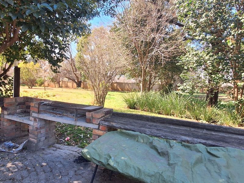 Outdoor entertainment area featuring a built-in brick braai and timber counter, set within a spacious garden environment.