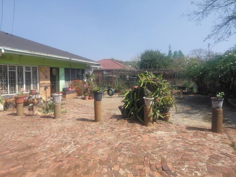 A rear exterior view of the house featuring a brick-paved courtyard, concrete pillars, and metal security bars on the windows.