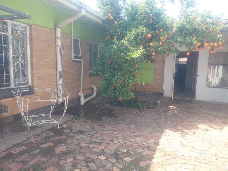 A rear exterior view of the property featuring brick paving, a mature fruit tree, and access to the interior via a security gate.