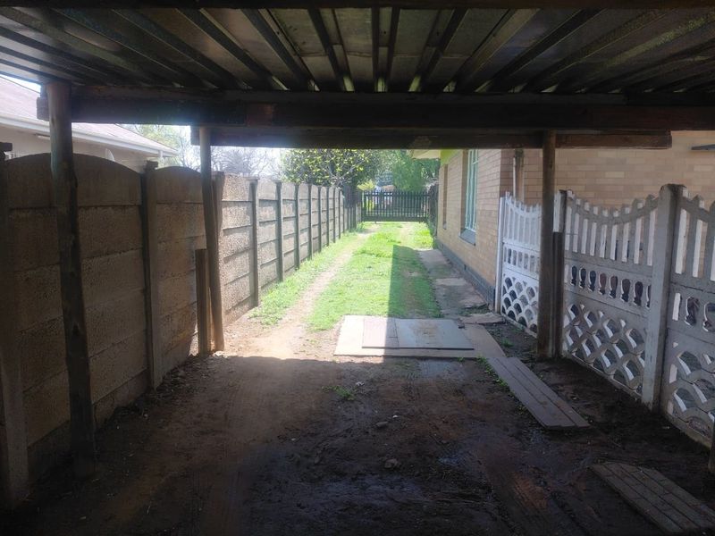 A covered outdoor area featuring a corrugated metal roof with timber supports, leading to a rear garden space enclosed by precast concrete walls.