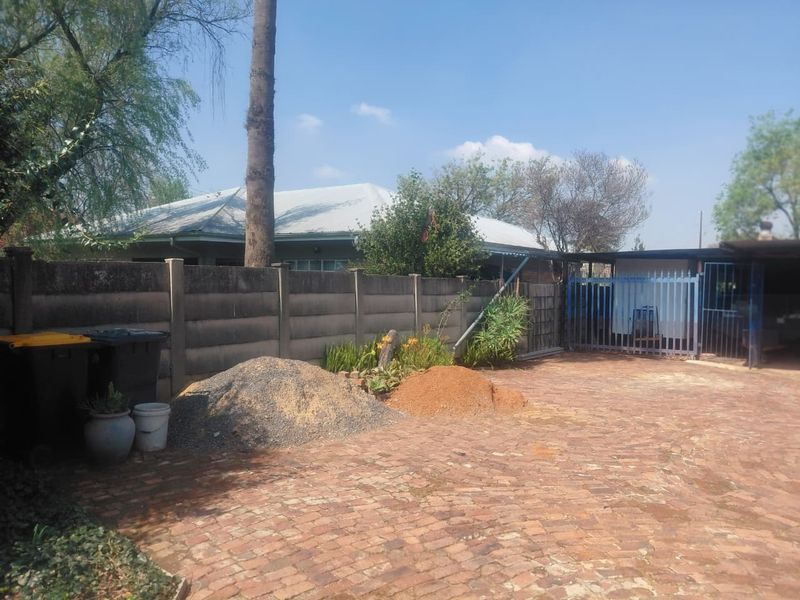 Rear exterior area featuring a brick paved driveway, precast concrete boundary wall, and metal security gate with an adjacent carport structure.