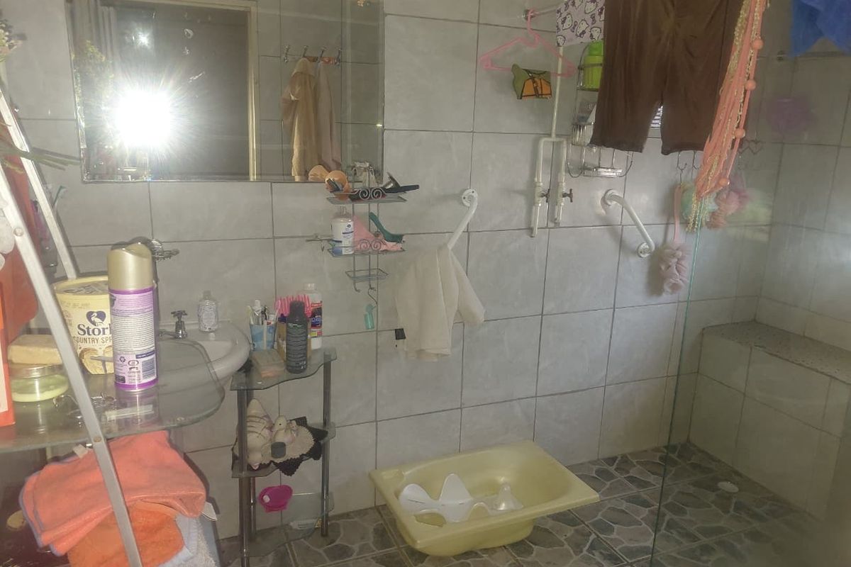 A functional bathroom featuring a walk-in shower with grab rails, wall-mounted basin, and tiled finishes throughout.
