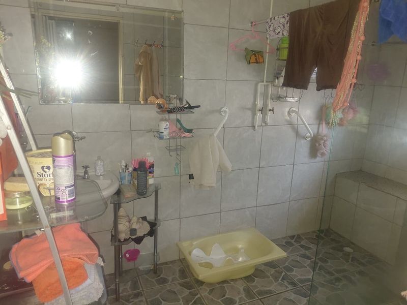A functional bathroom featuring a walk-in shower with grab rails, wall-mounted basin, and tiled finishes throughout.