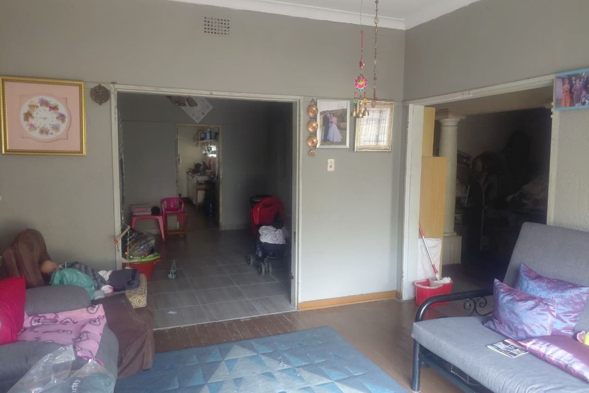 A living room area featuring a mix of wooden and tiled flooring, with an open archway leading to an adjacent space.