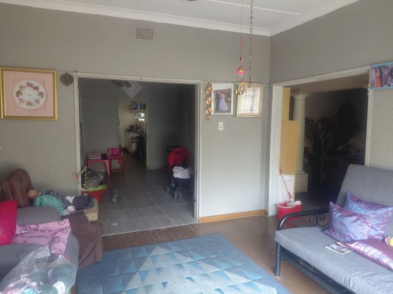 A living room area featuring a mix of wooden and tiled flooring, with an open archway leading to an adjacent space.