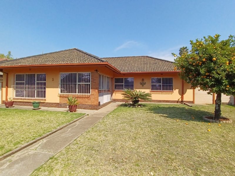 Front view of a single-story brick house featuring a tiled roof, security bars on windows, and a front garden with a concrete walkway.