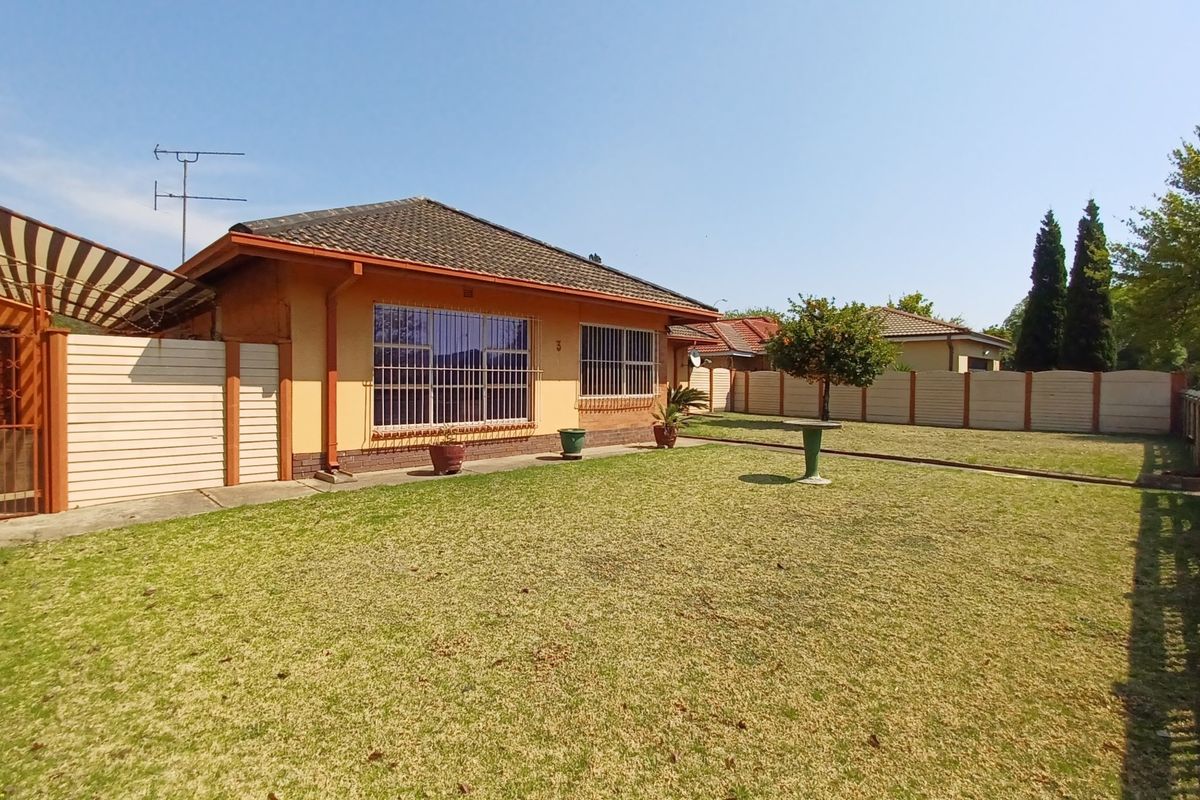 A view of the rear exterior of the house featuring a spacious lawn, perimeter walling, and security bars on the windows.