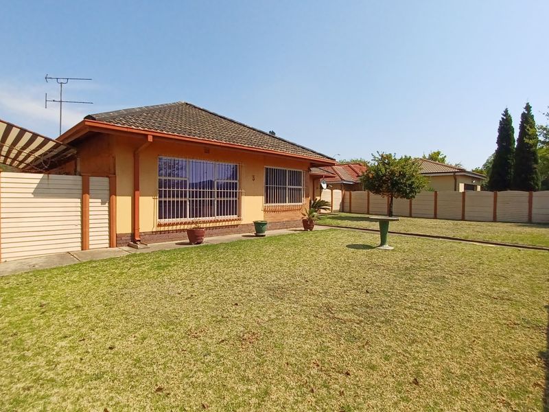 A view of the rear exterior of the house featuring a spacious lawn, perimeter walling, and security bars on the windows.