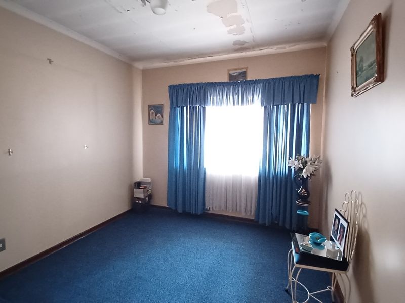 A bedroom featuring blue carpeting and a window with curtains, requiring ceiling repairs and cosmetic updates to improve the overall condition.