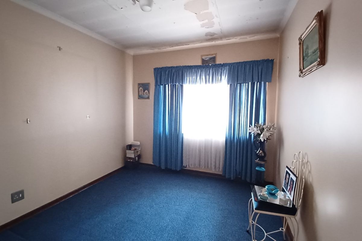 A bedroom featuring blue carpeting and a window with curtains, requiring ceiling repairs and cosmetic updates to improve the overall condition.