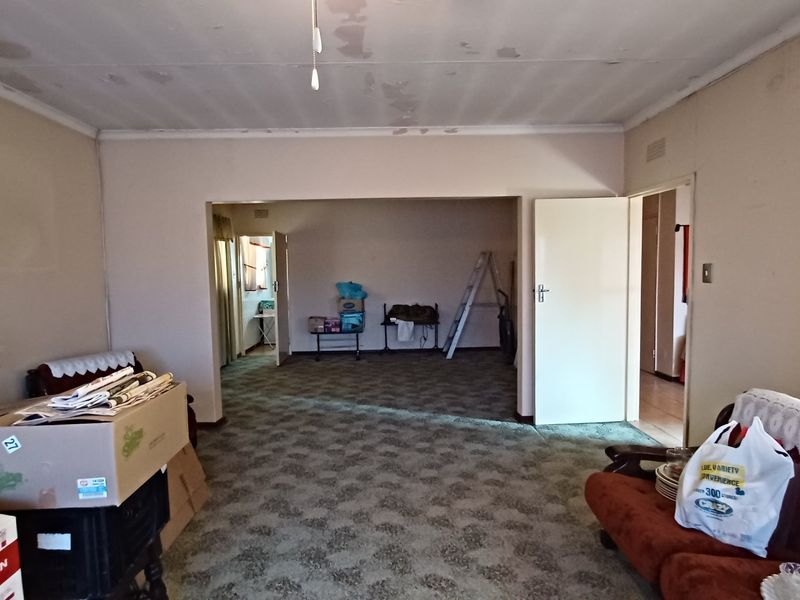 Spacious living area featuring carpeted flooring and ceiling detailing, requiring cosmetic updates and ceiling repairs.