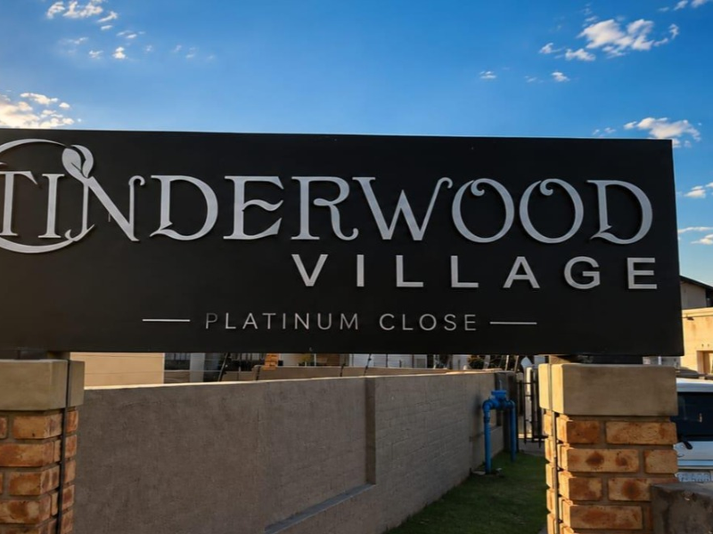 Entrance signage for Tinderwood Village, featuring a modern black sign mounted on brick pillars with perimeter wall and electric fencing.