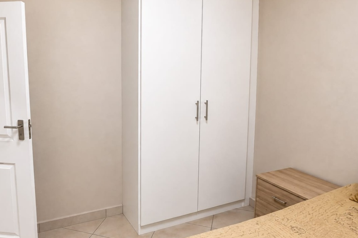 A clean bedroom featuring a white built-in wardrobe, neutral wall finishes, and tiled flooring.
