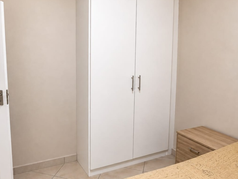 A clean bedroom featuring a white built-in wardrobe, neutral wall finishes, and tiled flooring.