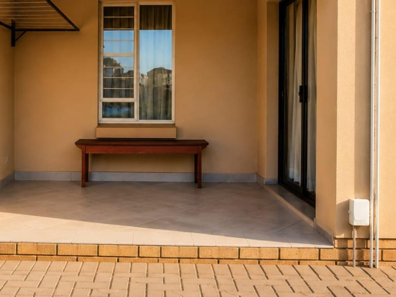 A clean, covered patio area featuring tiled flooring, a sliding glass door entrance, and a wall-mounted drying rack, providing a functional outdoor space.