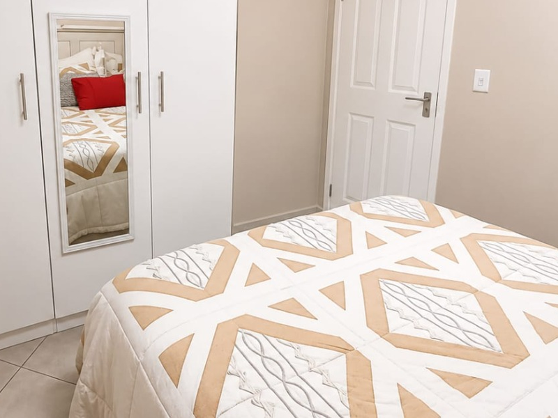 A well-maintained bedroom featuring built-in wardrobes with a mirrored panel, neutral wall tones, and tiled flooring.