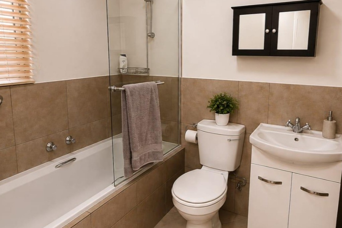 A functional bathroom featuring a bathtub with a glass screen, a vanity unit with a basin, and a wall-mounted medicine cabinet.