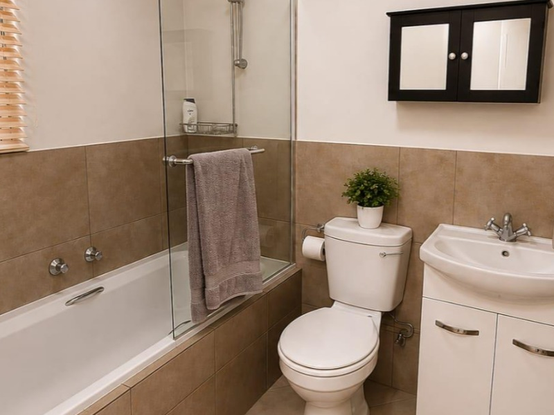 A functional bathroom featuring a bathtub with a glass screen, a vanity unit with a basin, and a wall-mounted medicine cabinet.