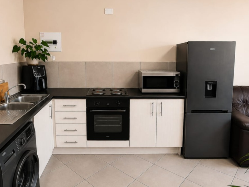 Compact open-plan kitchen area featuring modern cabinetry, dark countertops, integrated oven and hob, and tiled flooring, seamlessly connected to the living space.