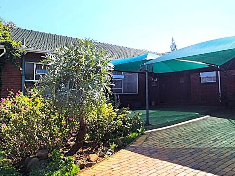 A rear view of the property featuring a brick facade, tiled roof, paved driveway area, and a large green shade sail for outdoor coverage.