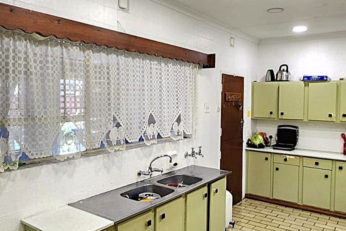 A functional kitchen featuring dated cabinetry, a double stainless steel sink, and tiled splashbacks, offering potential for a modern renovation.