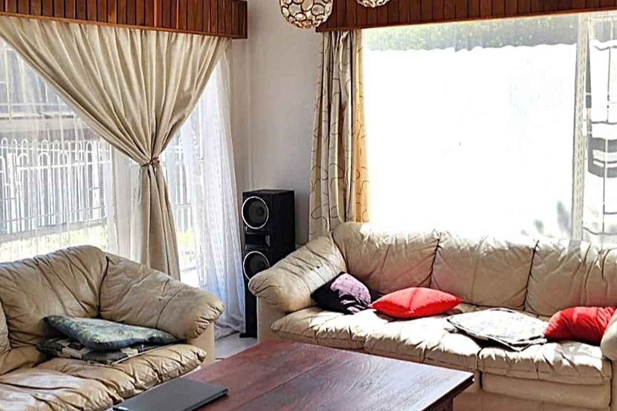 A living room featuring large windows with security bars and decorative timber ceiling trim, providing a bright and functional space.