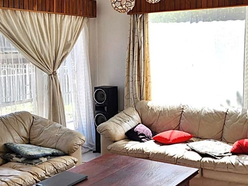 A living room featuring large windows with security bars and decorative timber ceiling trim, providing a bright and functional space.