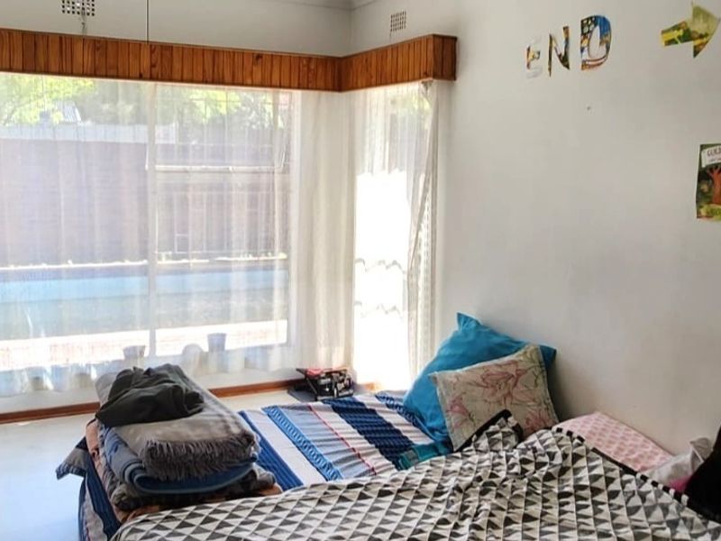 A bedroom featuring a large corner window with a timber pelmet, providing natural light and views of the exterior pool area.