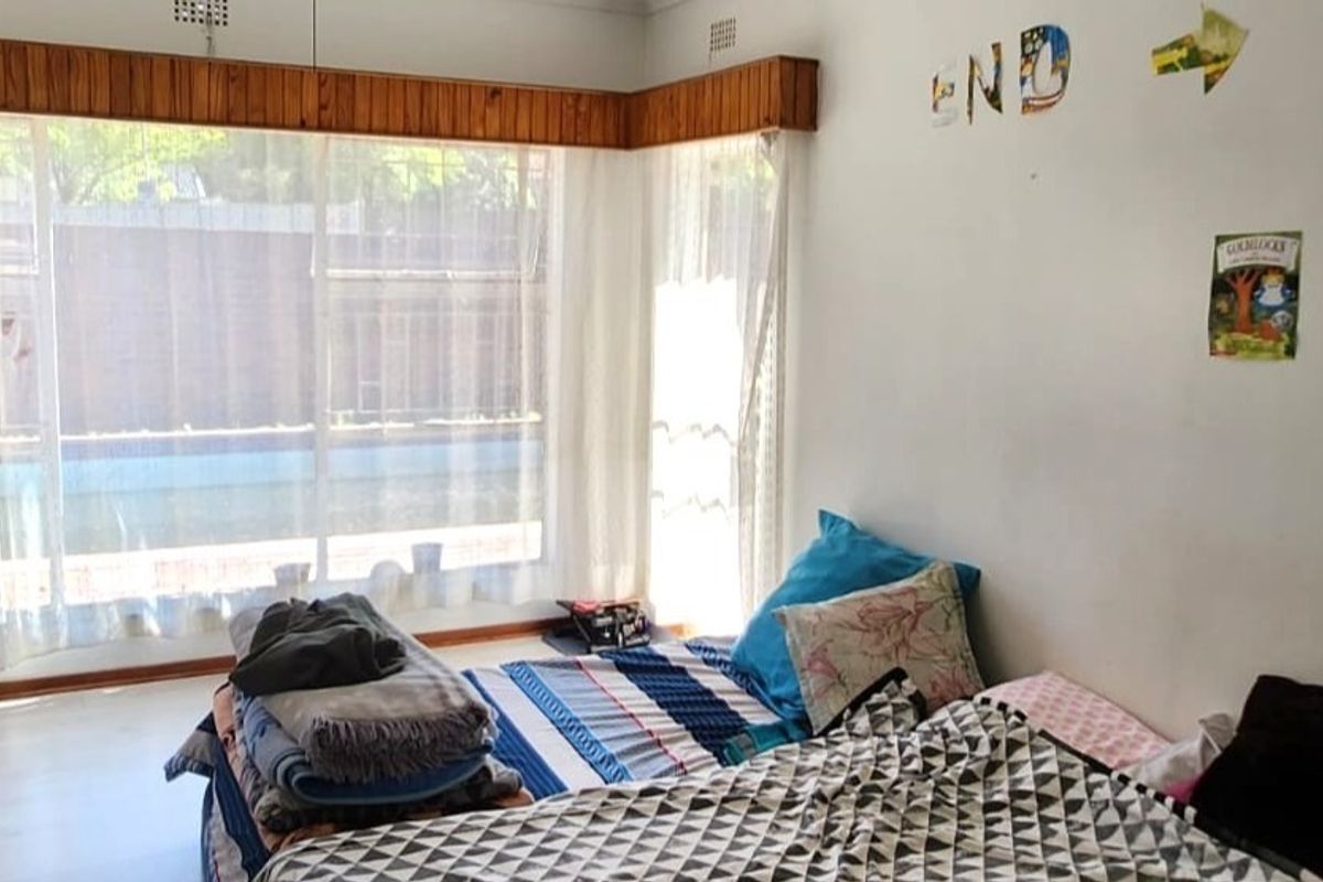 A bedroom featuring a large corner window with a timber pelmet, providing natural light and views of the exterior pool area.
